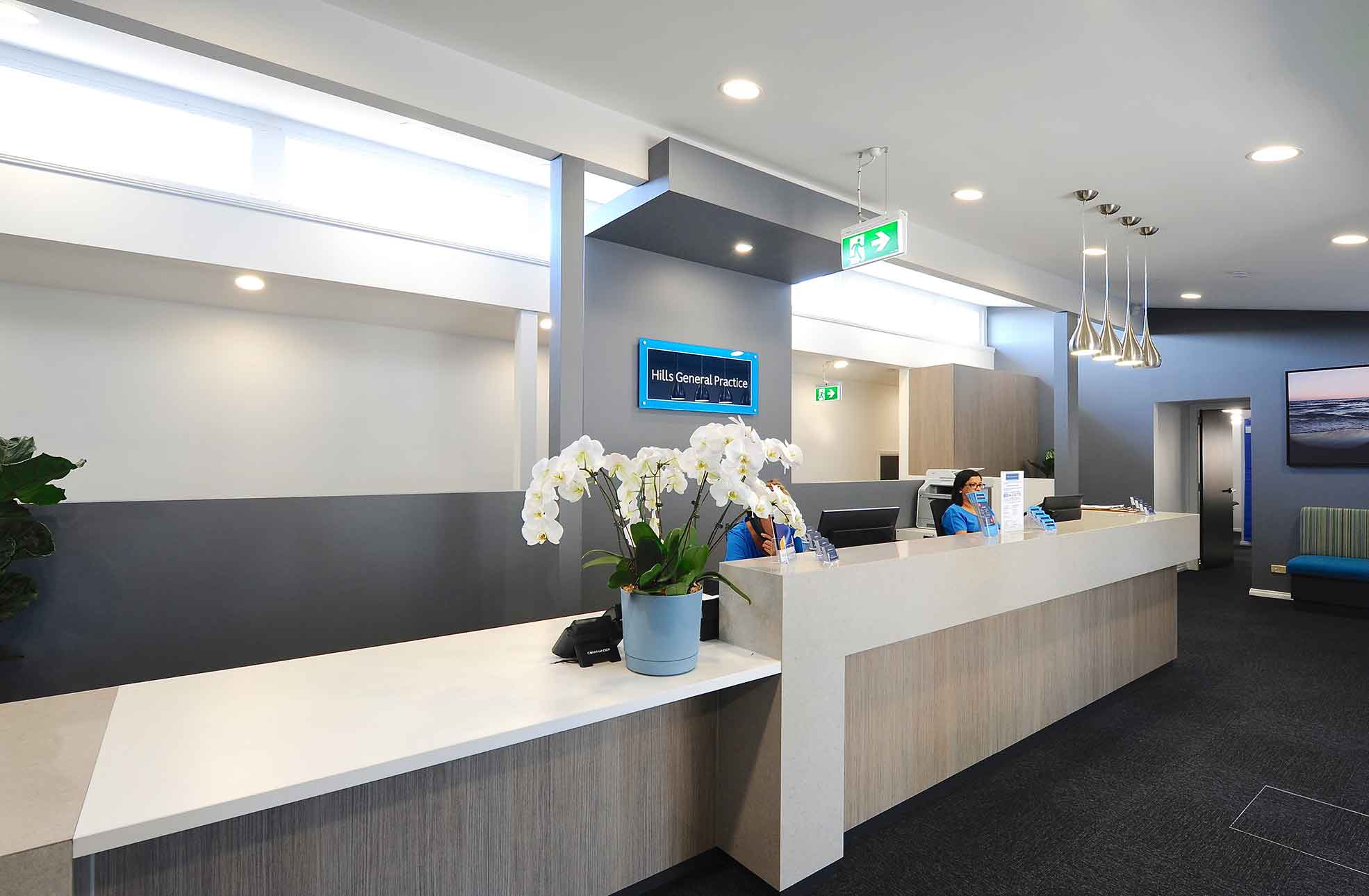 Medical centre fitout, refurbishment,  receptionist behind reception desk that has white flowers in blue pot